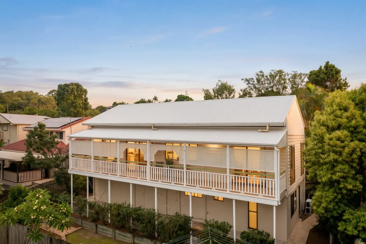 A classic Queenslander home with wrap-around verandah and lush green gardens under a clear blue sky in Sherwood — the character streets Ray White has served for 100 years